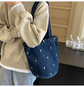 Détail du sac seau en denim bleu foncé avec broderies florales et large bandoulière