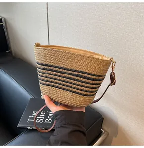 Macro detail of striped straw bucket bag with dark brown leather strap and gold hooks
