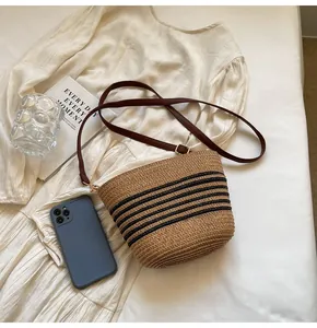 Detail of woven straw bucket bag with black stripes and brown leather shoulder strap