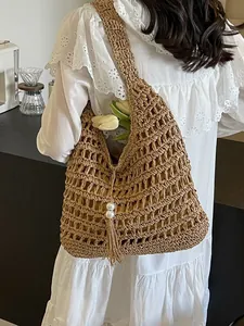 Sac cabas en paille ajourée style bohème avec pompon et perles porté par un mannequin