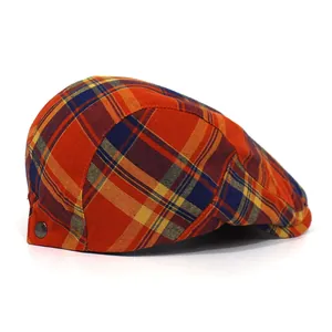 Detail of red and orange plaid flat cap featuring a side metal snap button and woven texture