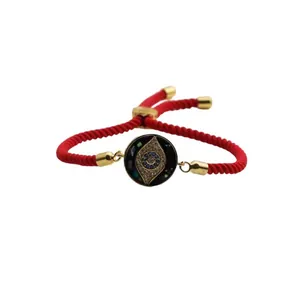 Macro detail of red woven rope bracelet with gold evil eye charm and adjustable toggle