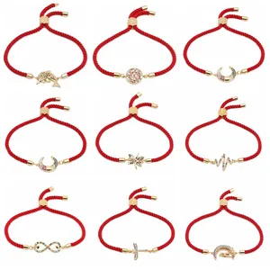 Dettaglio di braccialetti regolabili in corda rossa con ciondoli d'oro e zirconi