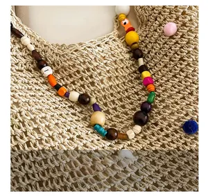 Detail of colorful beads and wooden charms on a beige woven straw beach shoulder bag