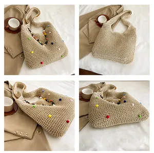 Detail of beige straw tote bag featuring multi-colored pom poms and beaded shoulder strap