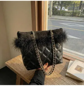Detail of black quilted shoulder bag with feather trim and metal chain strap on a bench