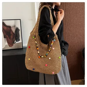 Detail of straw woven tote bag featuring colorful pompoms and beaded shoulder strap