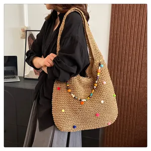 Detail of straw woven tote bag featuring colorful pom-poms and beaded charm accessories