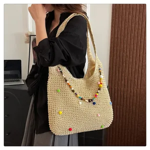 Detail of hand-woven straw shoulder bag with colorful beads and decorative plush pom-poms