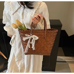 Detail of hand-woven brown tote bag featuring lace bow with pearls and heart pendant