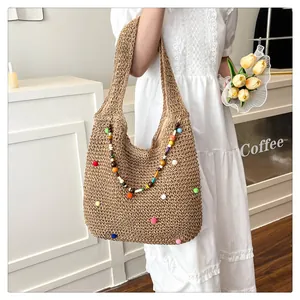 Close-up of woven straw beach bag featuring colorful pom-poms and decorative wooden beads