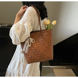 Macro detail of brown straw tote bag featuring white lace and pearl bow charm with tulips