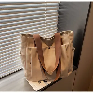 Detail of canvas tote bag showing side pocket, brown handles, and metal snap button
