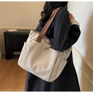Detail of reinforced brown shoulder straps and side pockets on a white canvas tote bag