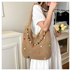 Detail of colorful pom-poms and beaded charm on the khaki straw woven tote beach bag