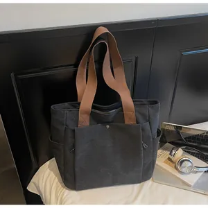 Detail of black canvas tote bag showing front pocket with metal buckle and brown strap
