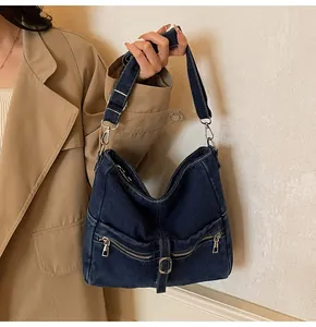 Detail of dark blue denim shoulder bag featuring dual zipper pockets and leather buckle