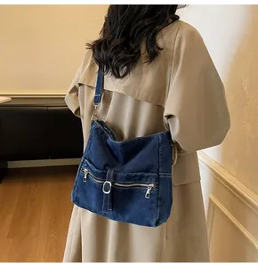 Detail of vintage blue denim crossbody bag with silver zippers shown on a beige trench coat