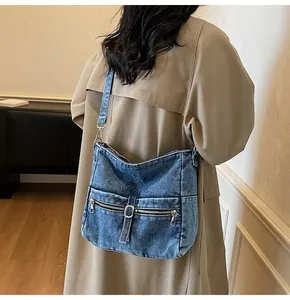Detail of vintage washed denim crossbody bag with dual zipper pockets and metal buckle