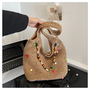 Close-up of straw tote bag featuring colorful pom-poms and rainbow beaded shoulder straps