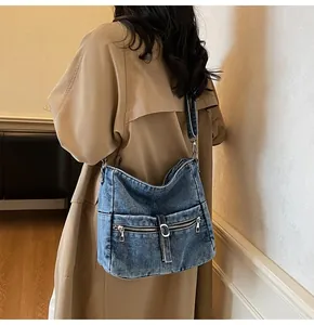 Detail of vintage washed denim crossbody bag with dual metal zipper pockets and buckle strap