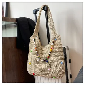 Detailed close-up of straw beach bag with colorful pom-poms and bead charms on suitcase
