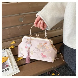 Close-up of pink silk embroidered handbag with golden handle, tassels and floral details