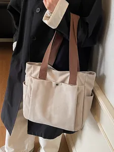 Minimalist beige canvas tote bag with brown handles and front pocket shown on model