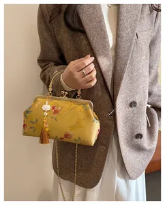 Detail of yellow shell bag with floral embroidery, metal frame, and tassel charm
