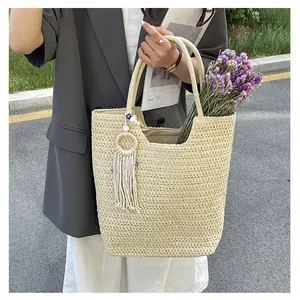 Détail du sac cabas en paille tissée avec pompon à anneau blanc et perle bleue
