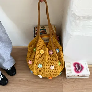 Close-up of a yellow hollow crochet bag with 3D floral accents and leather handles