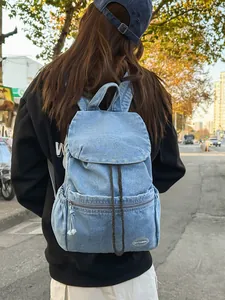 Vintage light blue denim backpack with drawstring closure and flap cover on outdoor street