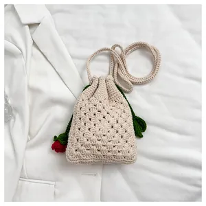 Primer plano de un bolso bandolera de ganchillo beige con detalle de rosa roja tejida