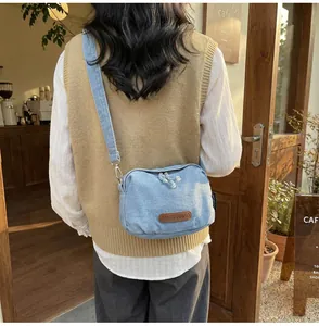 Dettaglio borsa a conchiglia in denim azzurro con toppa in pelle marrone e tracolla larga