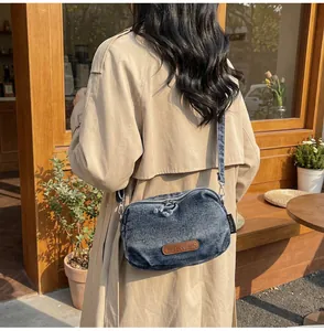 Dettaglio della borsa a tracolla in denim vintage blu con logo in pelle e cinturino