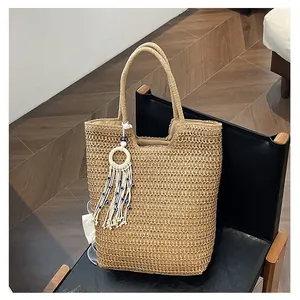 Détail du sac cabas en paille tressée avec pompon bleu sur une chaise noire chic