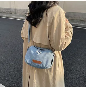 Dettaglio borsa a conchiglia in denim blu con doppia cerniera e logo in pelle su trench