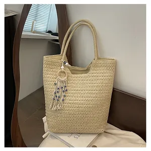 Gros plan d'un cabas tressé beige avec pompon à franges et perle d'œil bleu