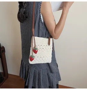 Detail der gewebten Strohtasche mit Blumenmuster, Erdbeeranhängern und braunem Gurt