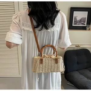 Detalle de bolso de paja con asa de bambú y cierre de cordón sobre vestido blanco