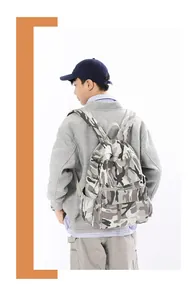 Male model wearing gray camo canvas backpack featuring large main pocket and front pouch