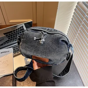 Dettaglio della borsa in denim blu con texture lavata retrò e toppa logo in pelle marrone