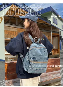 Detail of light blue washed denim backpack with multi-zipper pockets worn by a model