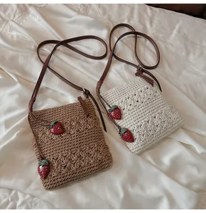 Detailansicht handgefertigter Strohtaschen mit roten Erdbeer-Anhängern und Blumenmustern