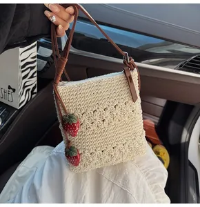 Detail der beige Häkeltasche mit roten Erdbeer-Anhängern und Leder-Schultergurt