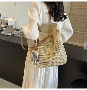 Detail of hand-woven straw tote bag featuring brown leather handles and evil eye tassel charm