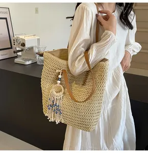 Detail of a straw tote bag with brown leather straps and an evil eye tassel charm