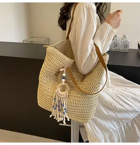 Detail of a beige woven straw tote bag with leather strap and evil eye tassel charm