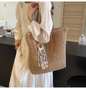 Detail of straw woven tote bag featuring brown leather handles and evil eye tassel charm
