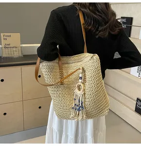 Detail of hollow woven straw tote with brown leather strap and evil eye tassel charm